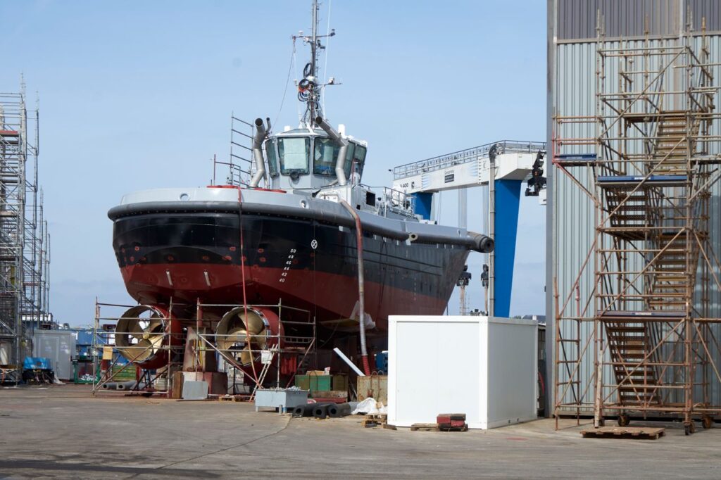 A large ship undergoing repairs in an industrial dockyard setting. Perfect for maritime industry themes.